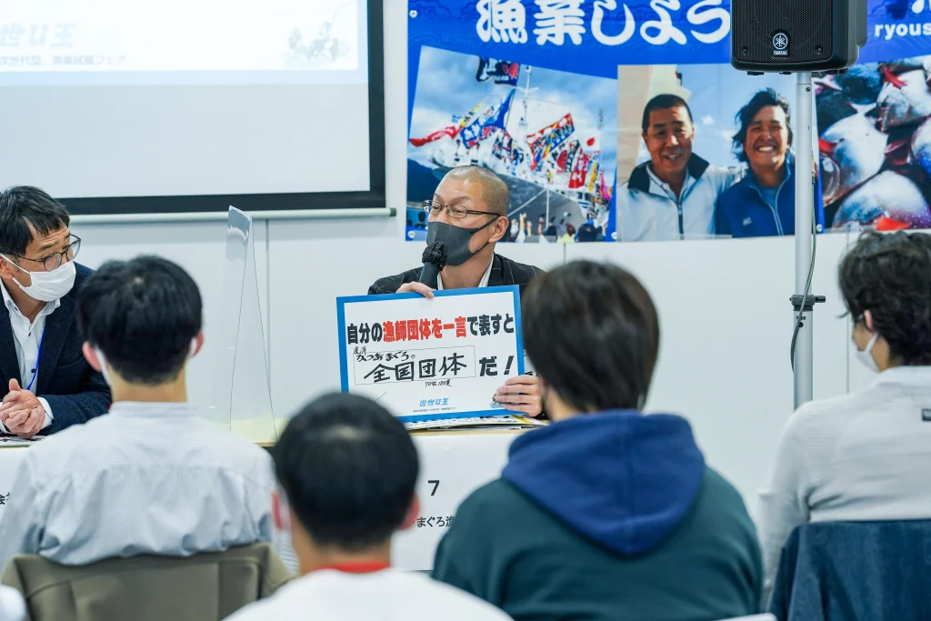 「自分の漁師団体を一言で表すと」のフリップを持って発表する男性